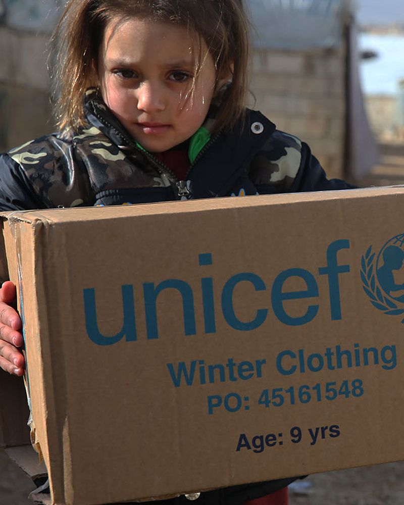 Bambina trasporta uno scatolone con aiuti UNICEF
