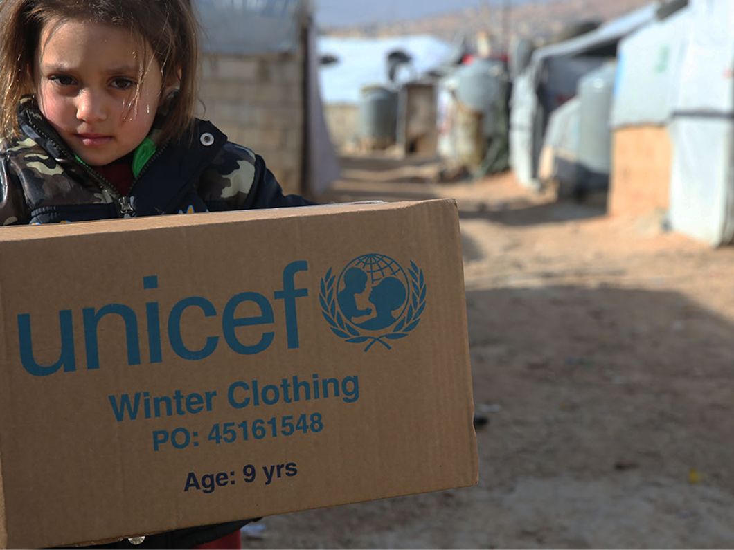 Bambina trasporta uno scatolone con aiuti UNICEF